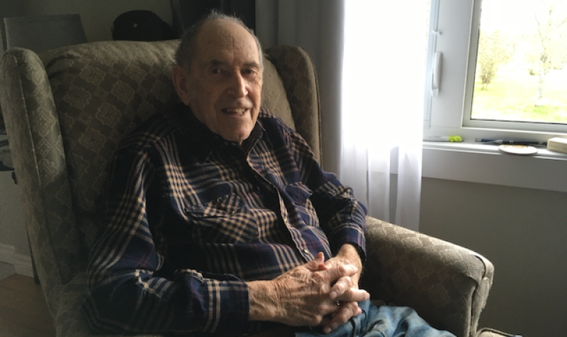 An older man sitting in an armchair beside a window.