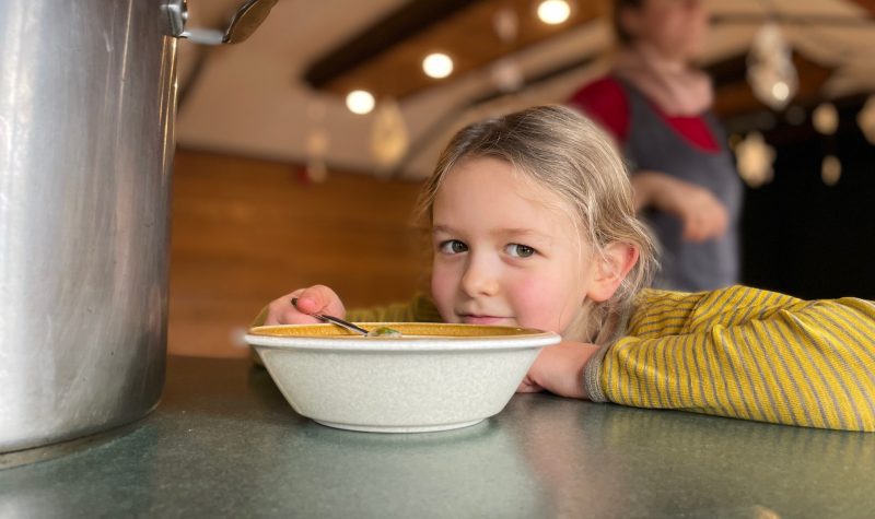 A child smiles by a big bowl of soup.