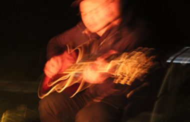 A long exposure photograph of a man playing guitar to fire light.