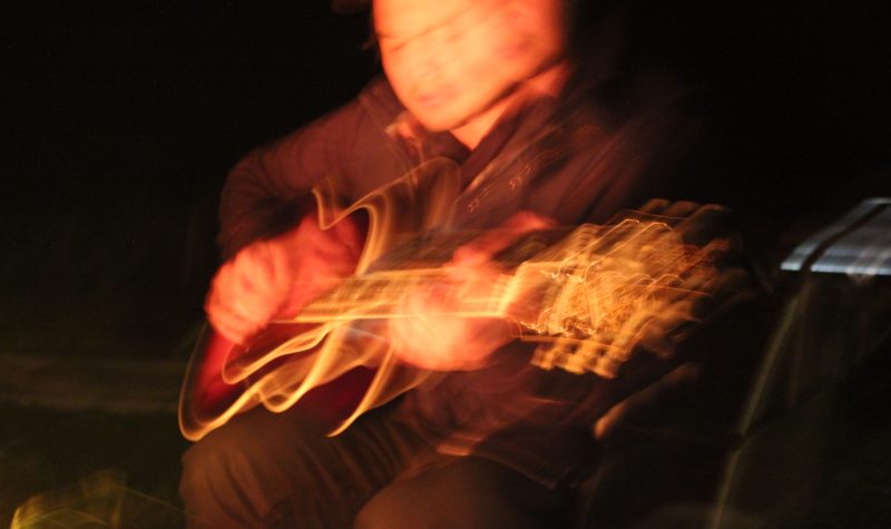 A long exposure photograph of a man playing guitar to fire light.