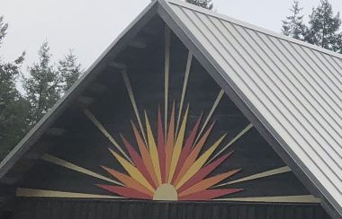 An image of a white, orange and yellow sunset is depicted on the peak of a wooden building.