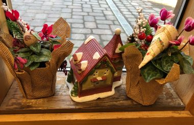 A Christmas window display adorns a Cortes Island post office. There's a small red house with red and white Christmas potted plants on either side.