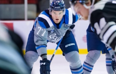 A hockey player on the ice in full uniform, surrounded by other players.