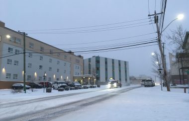 Une rue enneigée entre les édifices, sous un ciel gris