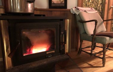 Black wood stove with fire burning and armchair featured in a rural living room.