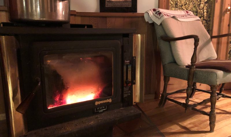 Black wood stove with fire burning and armchair featured in a rural living room.