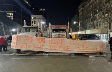 Trois camions sont au milieu d'une rue à Ottawa avec une banderole demandant d'ouvrir un pont.