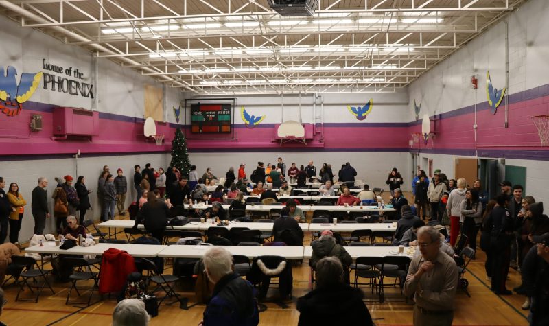 A wide shot of the Bent Arrow Gymnasium with people lined up all the way around the perimeter of the gym waiting for some soup and Bannock.
