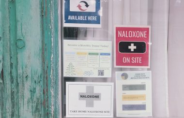 Signs posted on a window advertising Naloxone and harm reduction supplies.