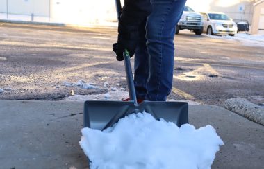 A chunk of snow being shoveled off of a sidewalk. Weather is clear and sunny