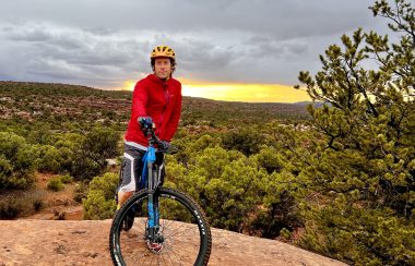 Man in red jacket posing on a mountain bike. Sunset in the background.