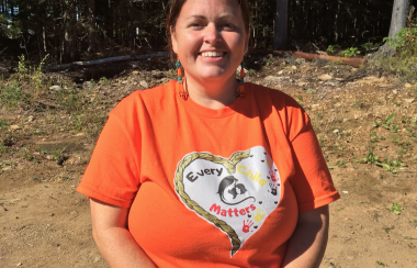 A woman standing wearing an orange shirt with a white heart on it.