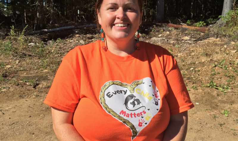 A woman standing wearing an orange shirt with a white heart on it.