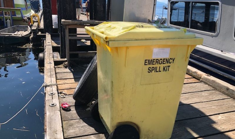 A yellow waste bin sits on a dock with boats tied up alongside.