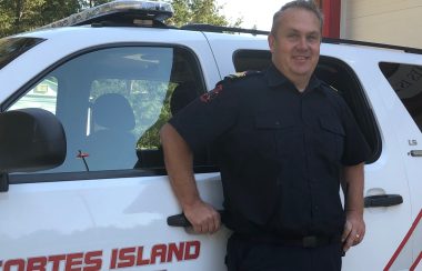 A man in a blue uniform leans against a fire department vehicle.