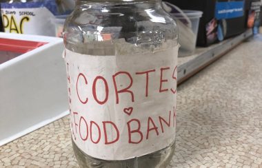 A glass donation jar with a white label and red writing sits on a store counter.