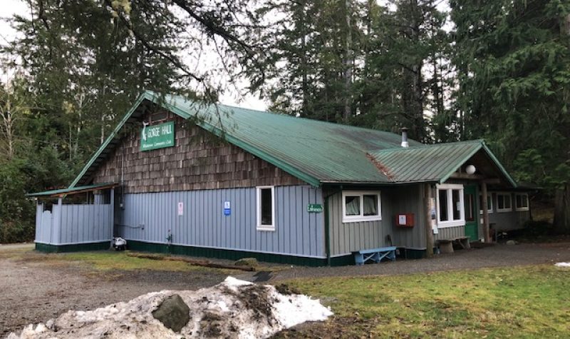 A one story wooden building with a green roof sits in a forested setting.