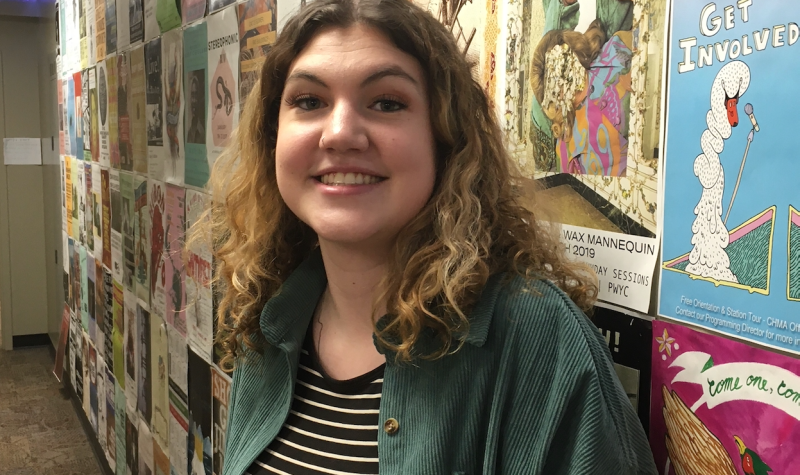 A young woman, smiling, standing in a hallway.