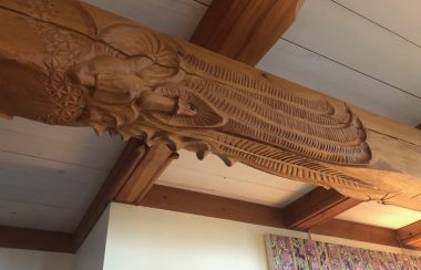 A wooden beam featuring an artist's carving sits below a white ceiling.