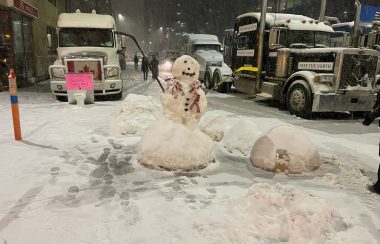 Deux bonhommes de neige au milieu de la rue en centre de ville d'Ottawa avec 2 camions.