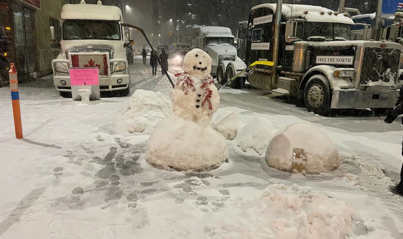 Deux bonhommes de neige au milieu de la rue en centre de ville d'Ottawa avec 2 camions.