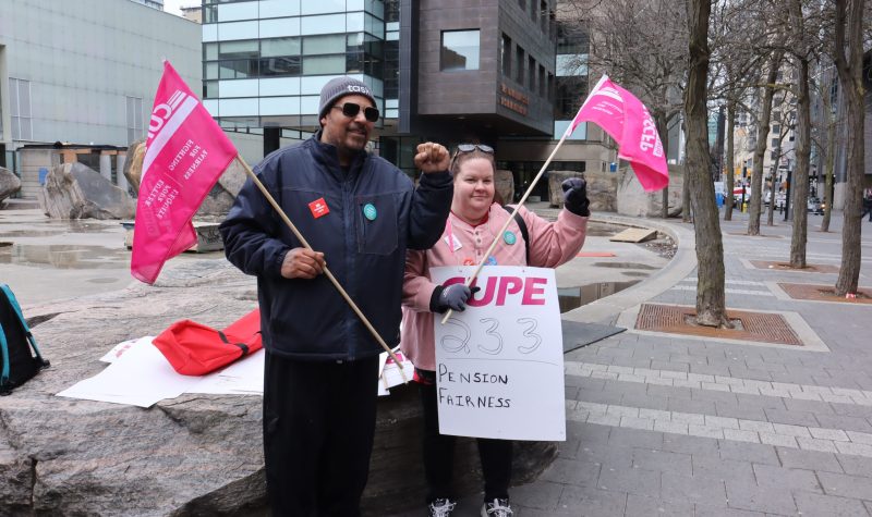 Cupe 233 vice-president and treasurer raising their left fists and carrying pink flags.