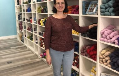 Miranda Holmes, owner & operator of String Theory Yarn, stands in front of a yarn display in her shop.