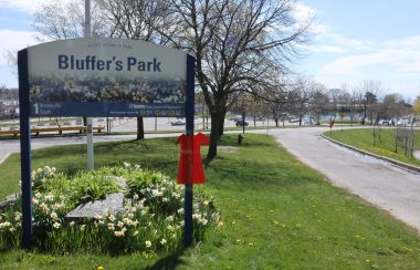 A sign for bluffers park with a cut out of a red dress taped to it