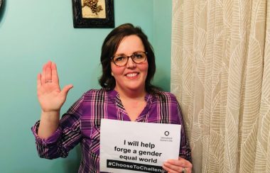 Helena Burke holding a sign about International Women's Day and holding a hand up to pledge