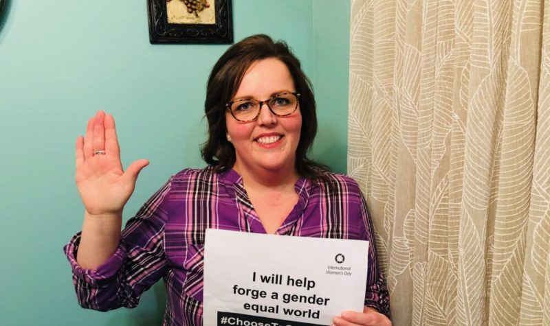 Helena Burke holding a sign about International Women's Day and holding a hand up to pledge