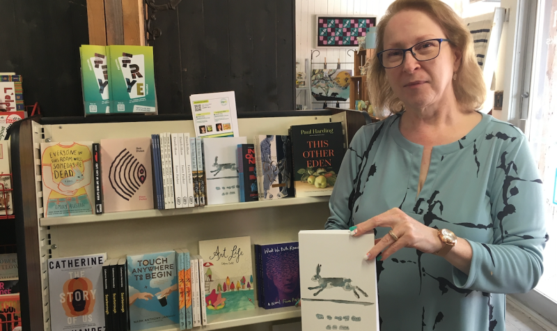 A woman stands holding a book in front of a book display full of other books