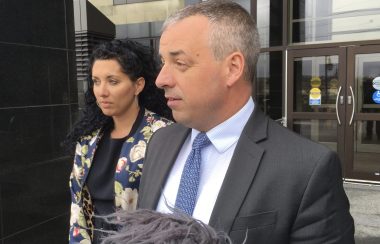 A woman and man standing outside a courthouse with mics pointed toward them.