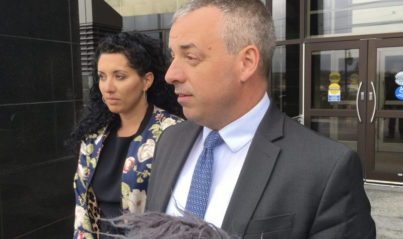 A woman and man standing outside a courthouse with mics pointed toward them.