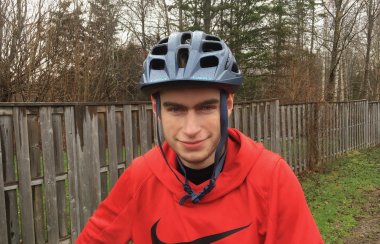 A young man wearing a red sweater and a bike helmet, smiling at camera