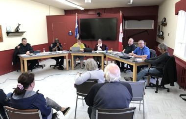 Les élus municipaux assis l'un à côté de l'autre à des tables en positions ovales dans une salle devant des citoyens.