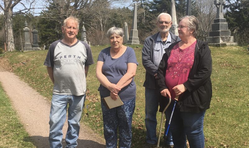 Four people stand together on a pathway in a cemetery