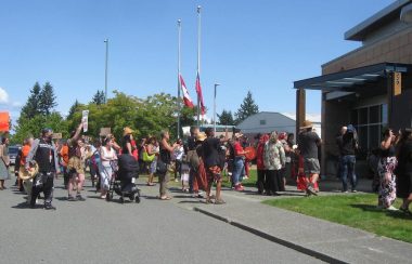 A crowd of Indigenous people, some with drums, heading for the front door of a police station