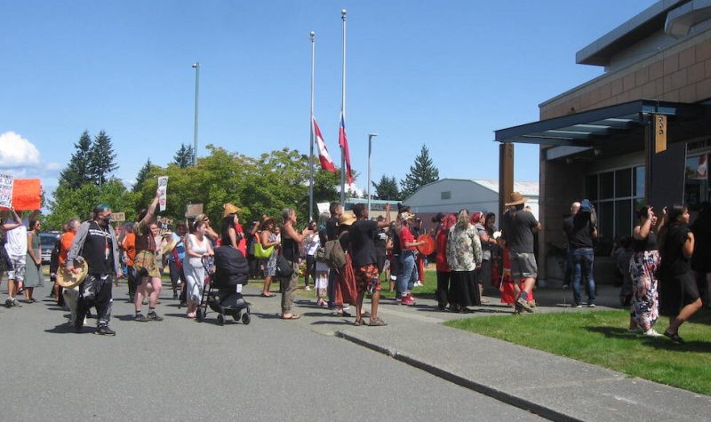 A crowd of Indigenous people, some with drums, heading for the front door of a police station