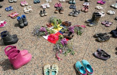 Childrens' shoes and flowers are arranged in a circle on pavement.