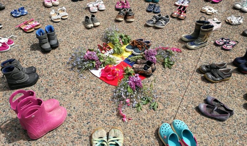 Childrens' shoes and flowers are arranged in a circle on pavement.