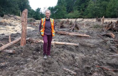 Woman standing in a dirt field full of sticks, logs and straw