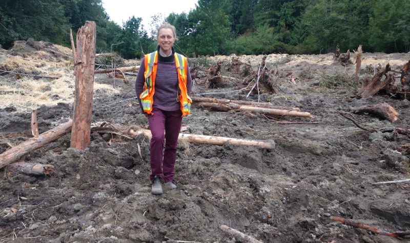 Woman standing in a dirt field full of sticks, logs and straw