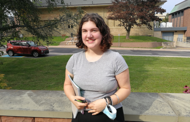 A young woman standing in front of a sandstone wall.