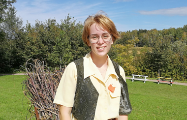 A young woman standing with a park in the background.