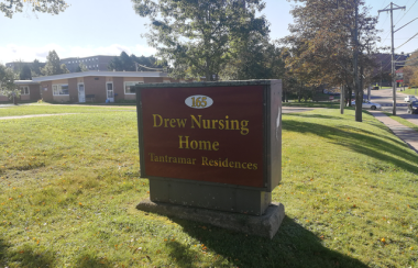 A sign with red background and gold lettering saying Drew Nursing Home, on a green lawn.