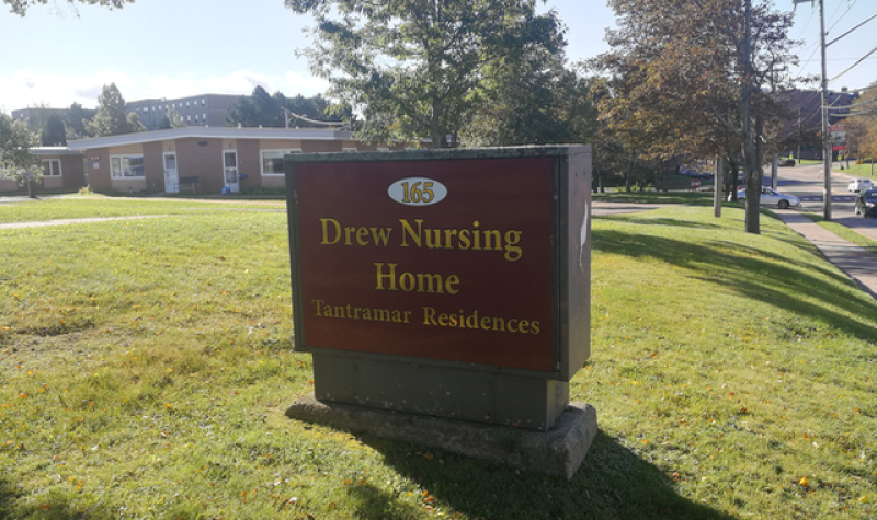 A sign with red background and gold lettering saying Drew Nursing Home, on a green lawn.