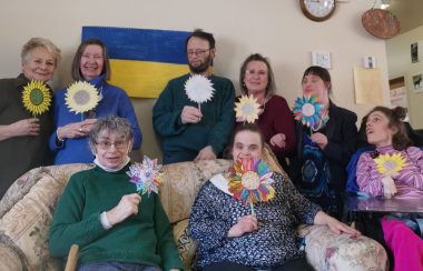 Scott and Samborsky with their clients. They are holding flowers that they made together with the Ukraine flag pictured behind them.