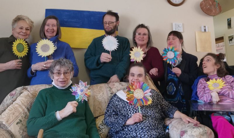 Scott and Samborsky with their clients. They are holding flowers that they made together with the Ukraine flag pictured behind them.