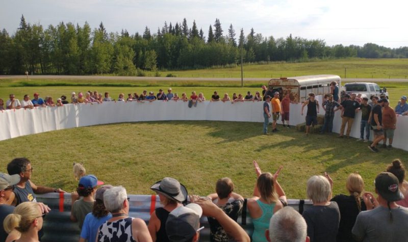 Une foule est amassée autour d'une arène circulaire, dans laquelle se trouve six participants.