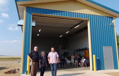 Dan Small, Darlene Beniuk et Dylan Maskalyk posent pour une photo devant la nouvelle infrastructure, à l'intérieur de laquelle se trouvent une vingtaine de personnes.